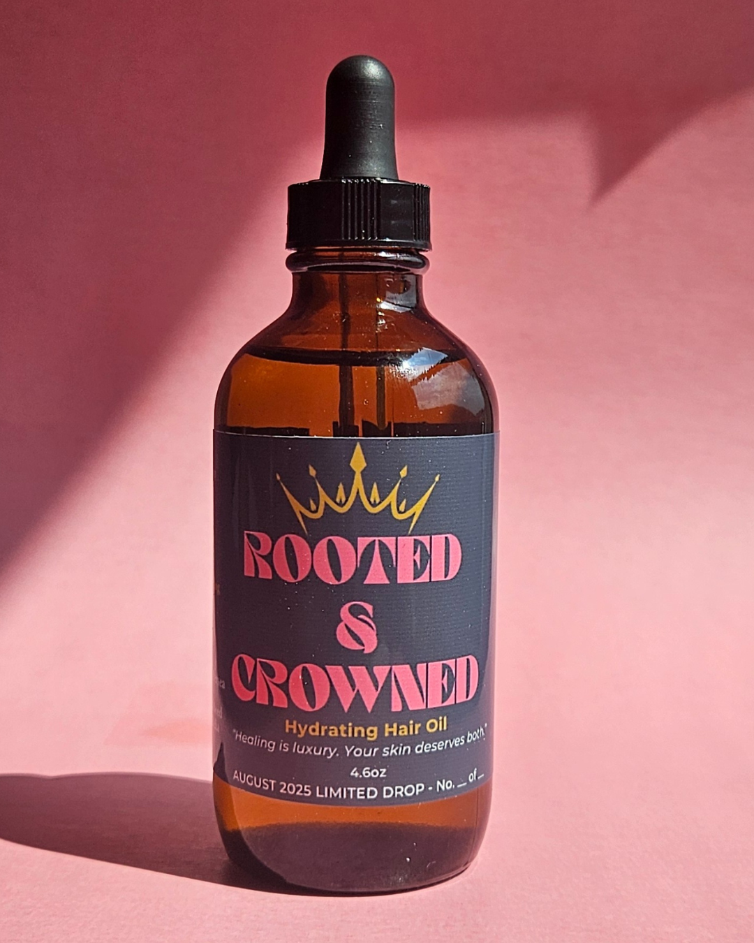 Hydrating Hair Oil by Rooted & Crowned in amber glass dropper bottle, photographed on a pink background for a luxe and modern product display.