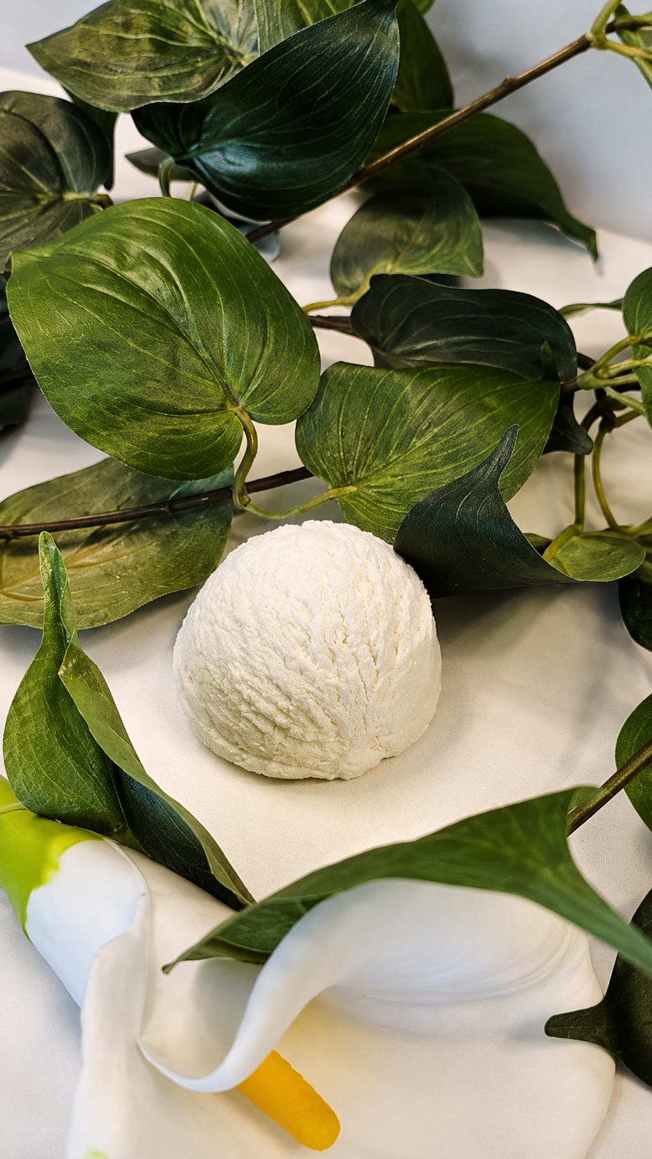 Botanical still life of by A’amia Coconut Milk Bath Scoops with soft green leaves and a white calla lily, showing the quiet fragrance-free bath ritual.