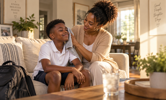 Black mother gently cooling down her son with a soft towel after a hot school day, with his backpack nearby in a warm, sunlit living room.